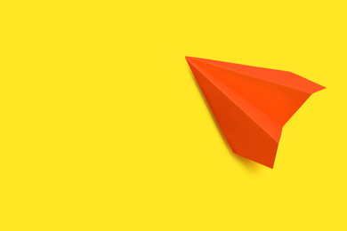 Photo of Orange paper plane on yellow background, top view. Space for text