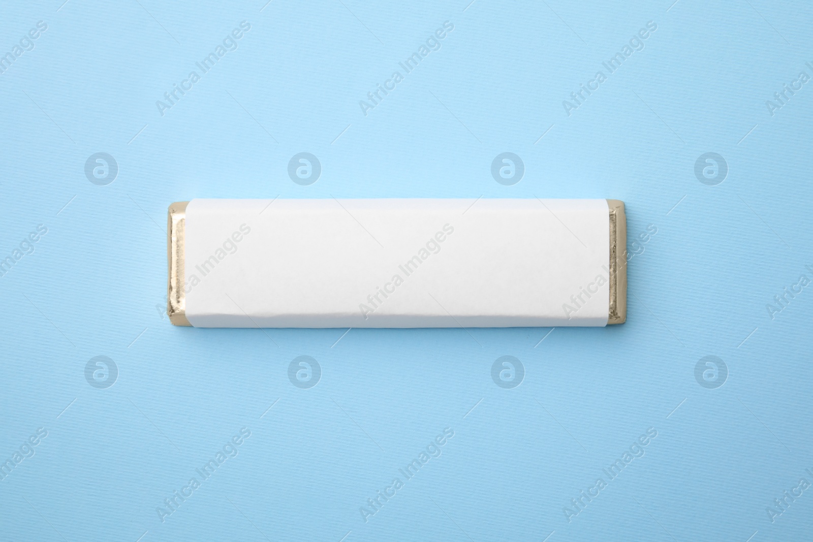 Photo of Tasty chocolate bar in package on light blue background, top view