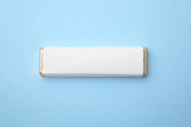 Tasty chocolate bar in package on light blue background, top view