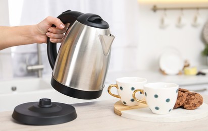 Woman with electric kettle in kitchen, closeup. Space for text