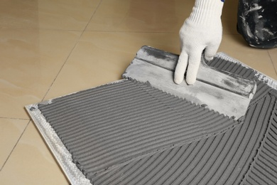 Worker spreading concrete over ceramic tile with spatula on floor, closeup. Space for text