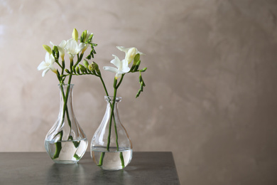 Beautiful freesia flowers in vases on grey table. Space for text