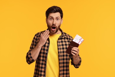 Surprised man with passport and tickets on yellow background