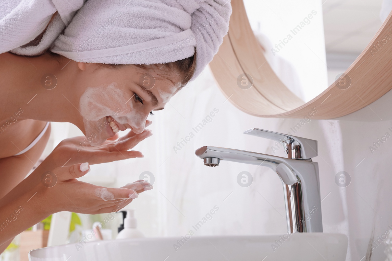 Photo of Beautiful teenage girl washing face with cleansing foam in bathroom. Skin care cosmetic