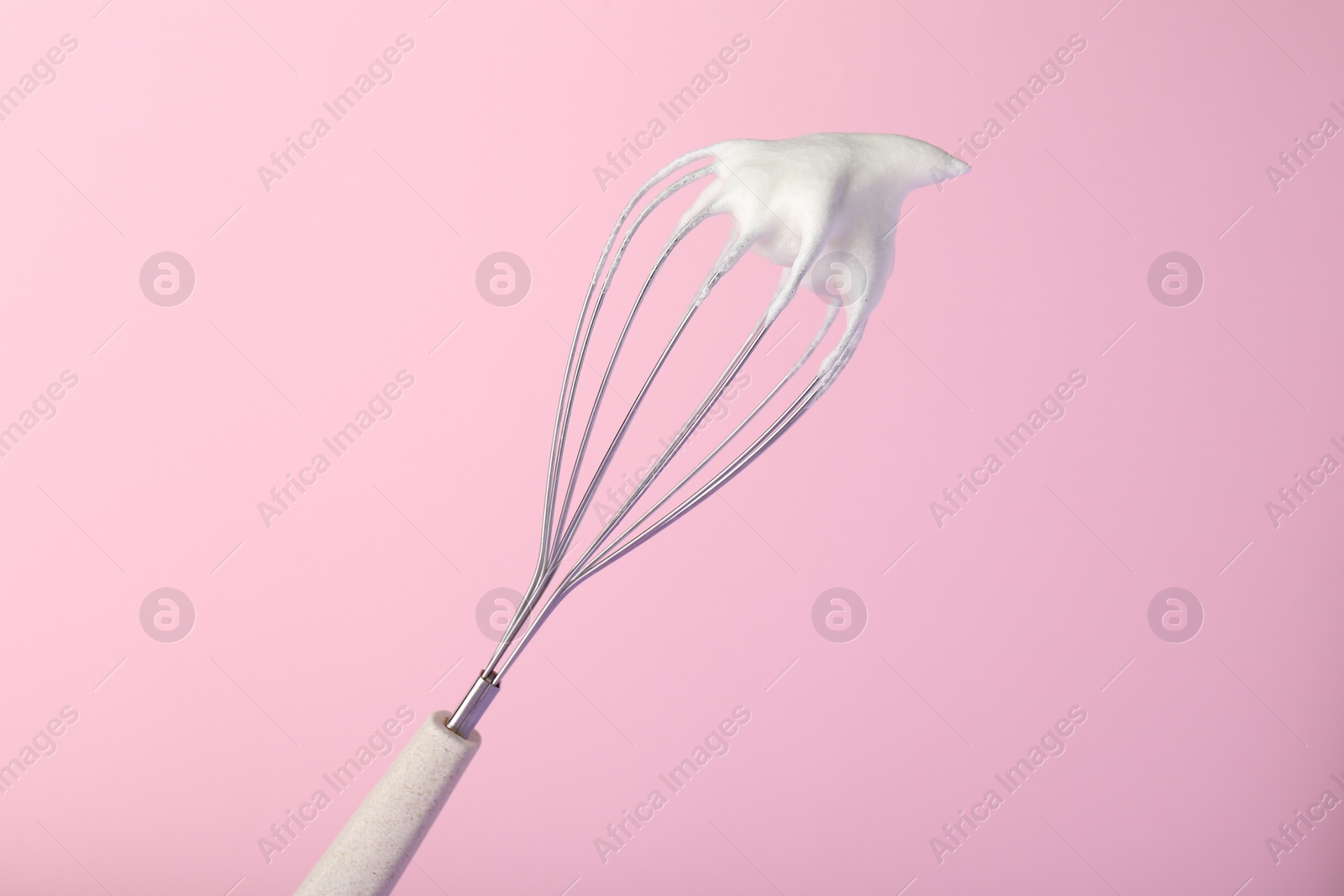 Photo of Whisk with whipped egg whites on pink background