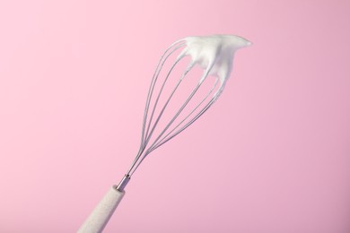 Whisk with whipped egg whites on pink background