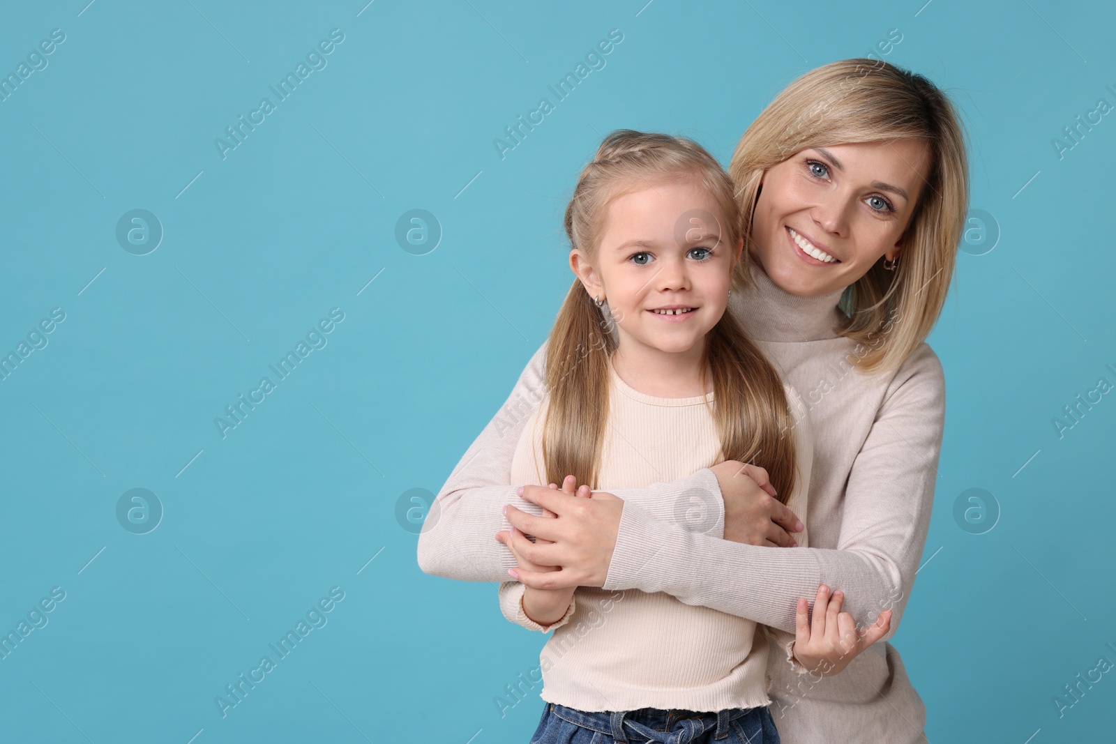 Photo of Mother hugging her happy daughter on light blue background. Space for text