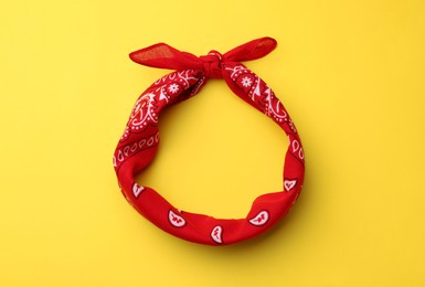 Photo of Tied red bandana with paisley pattern on yellow background, top view
