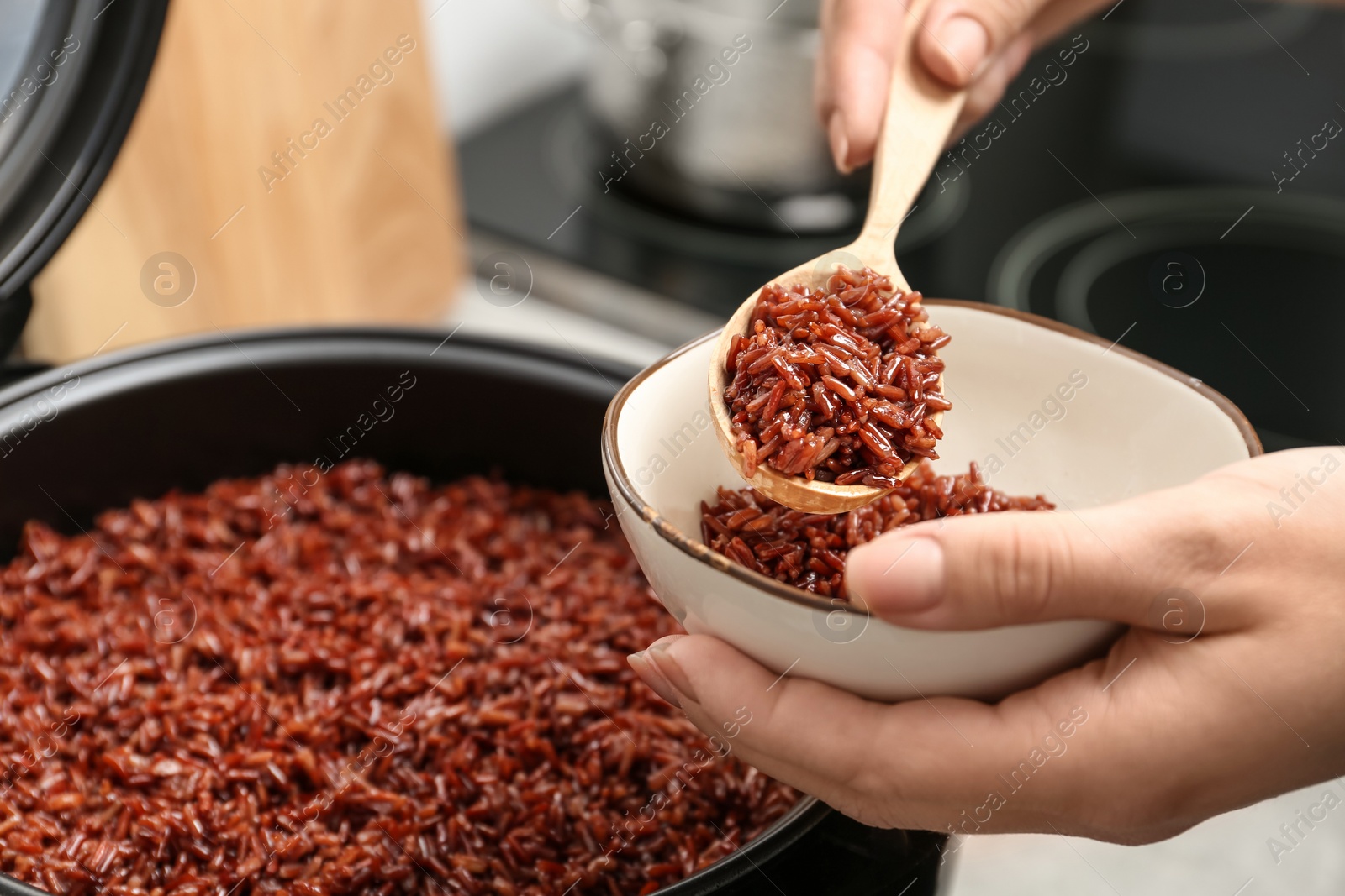 Photo of Woman putting brown rice into bowl from multi cooker in kitchen, closeup