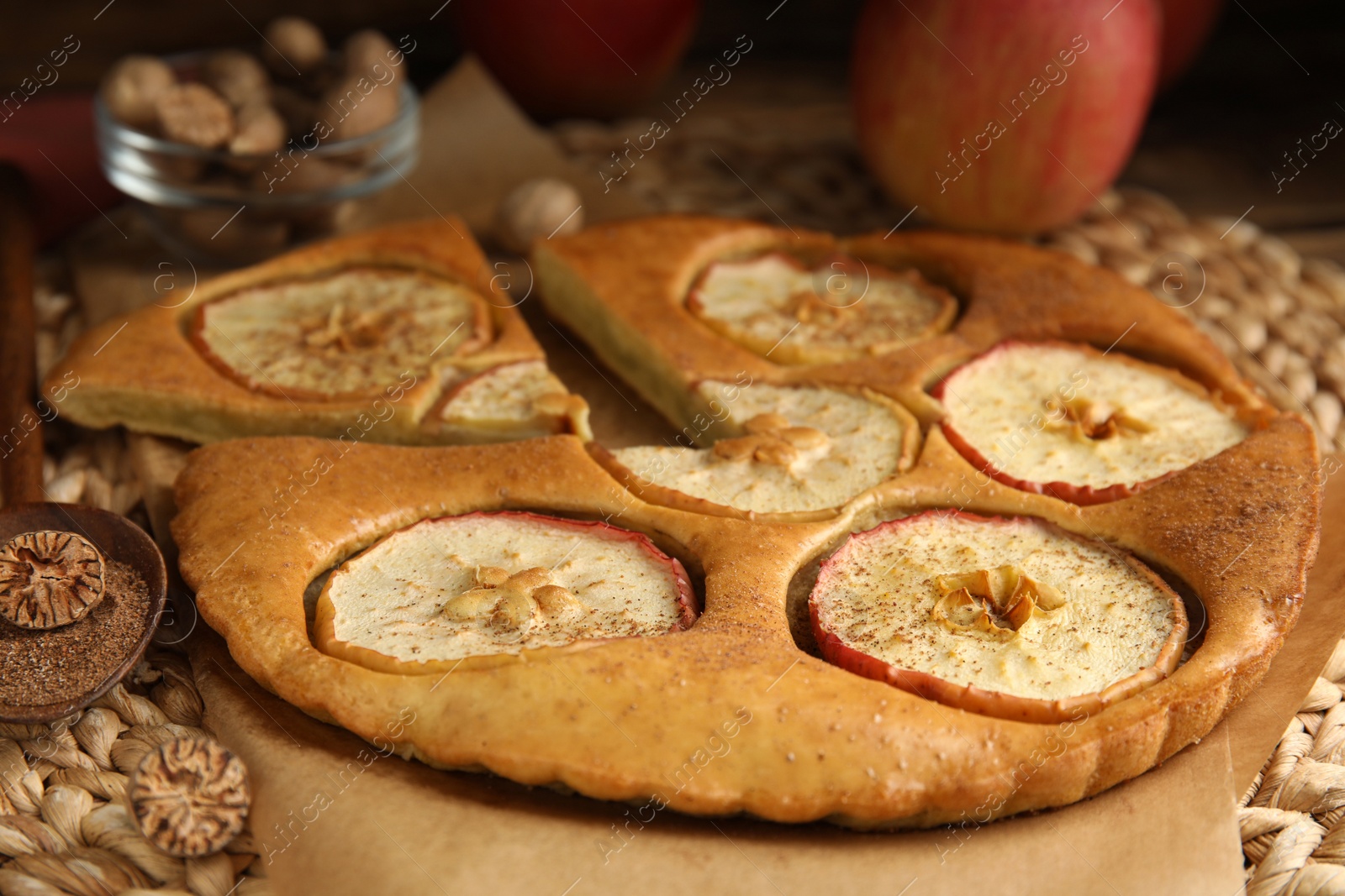 Photo of Nutmeg powder, seed and tasty apple pie on wicker mat, closeup