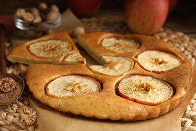 Nutmeg powder, seed and tasty apple pie on wicker mat, closeup