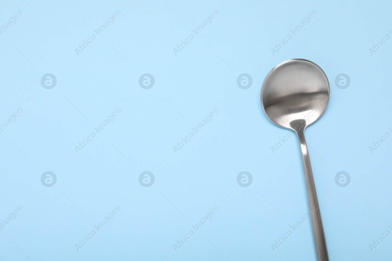 Photo of One shiny silver spoon on light blue background, top view. Space for text