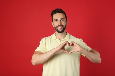 Photo of Happy man making heart with hands on red background