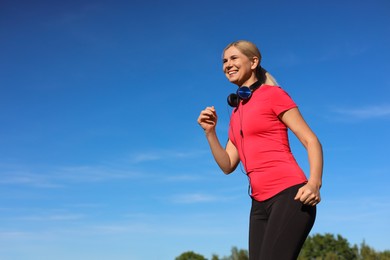 Woman with headphones running outdoors in morning, low angle view. Space for text