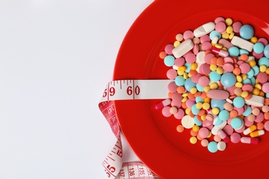 Photo of Plate with weight loss pills and measuring tape on white background, top view. Space for text