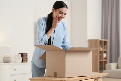 Photo of Happy young woman unpacking parcel at home. Internet shopping