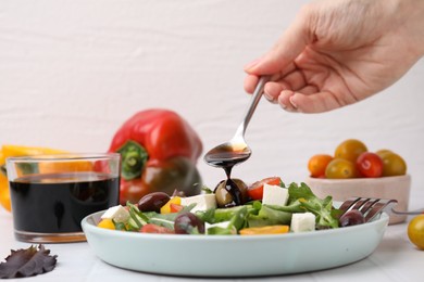 Woman pouring vinegar from spoon into plate with salad at white tiled table, closeup