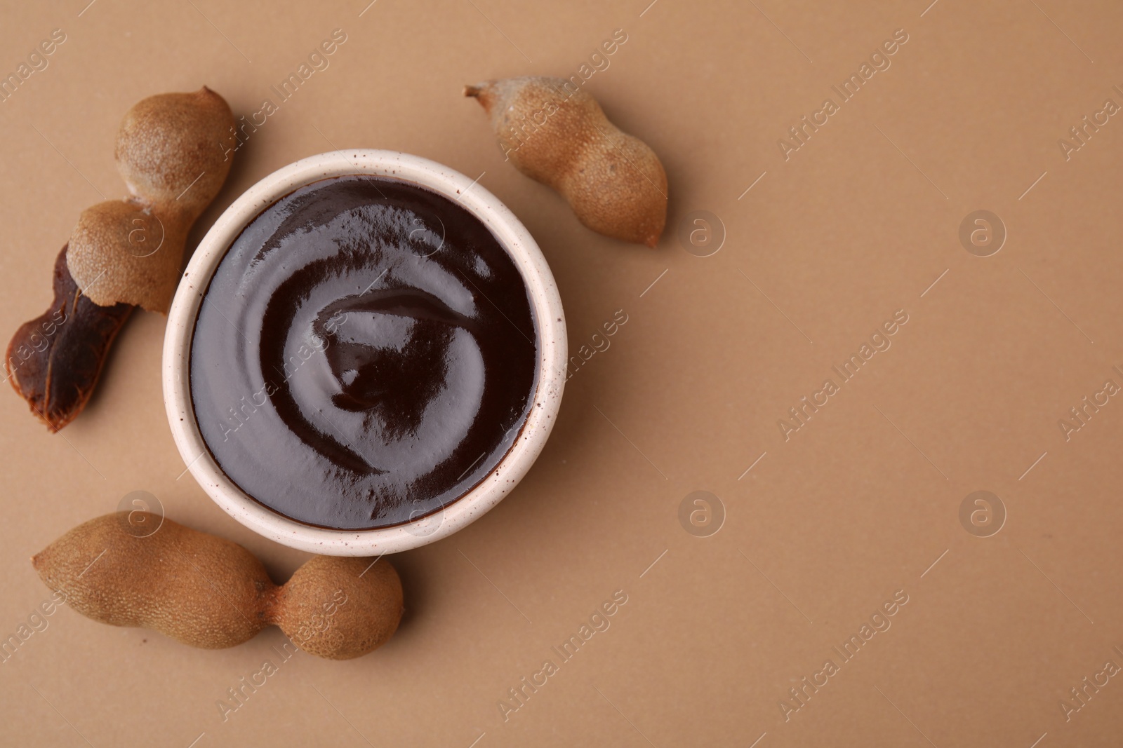 Bowl of tamarind sauce and fresh pods on light brown table, flat lay. Space for text Photo of Bowl of tamarind sauce and fresh pods on light brown table, flat lay. Space for text