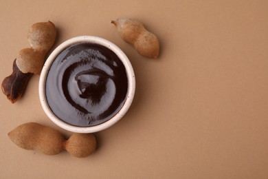 Photo of Bowl of tamarind sauce and fresh pods on light brown table, flat lay. Space for text