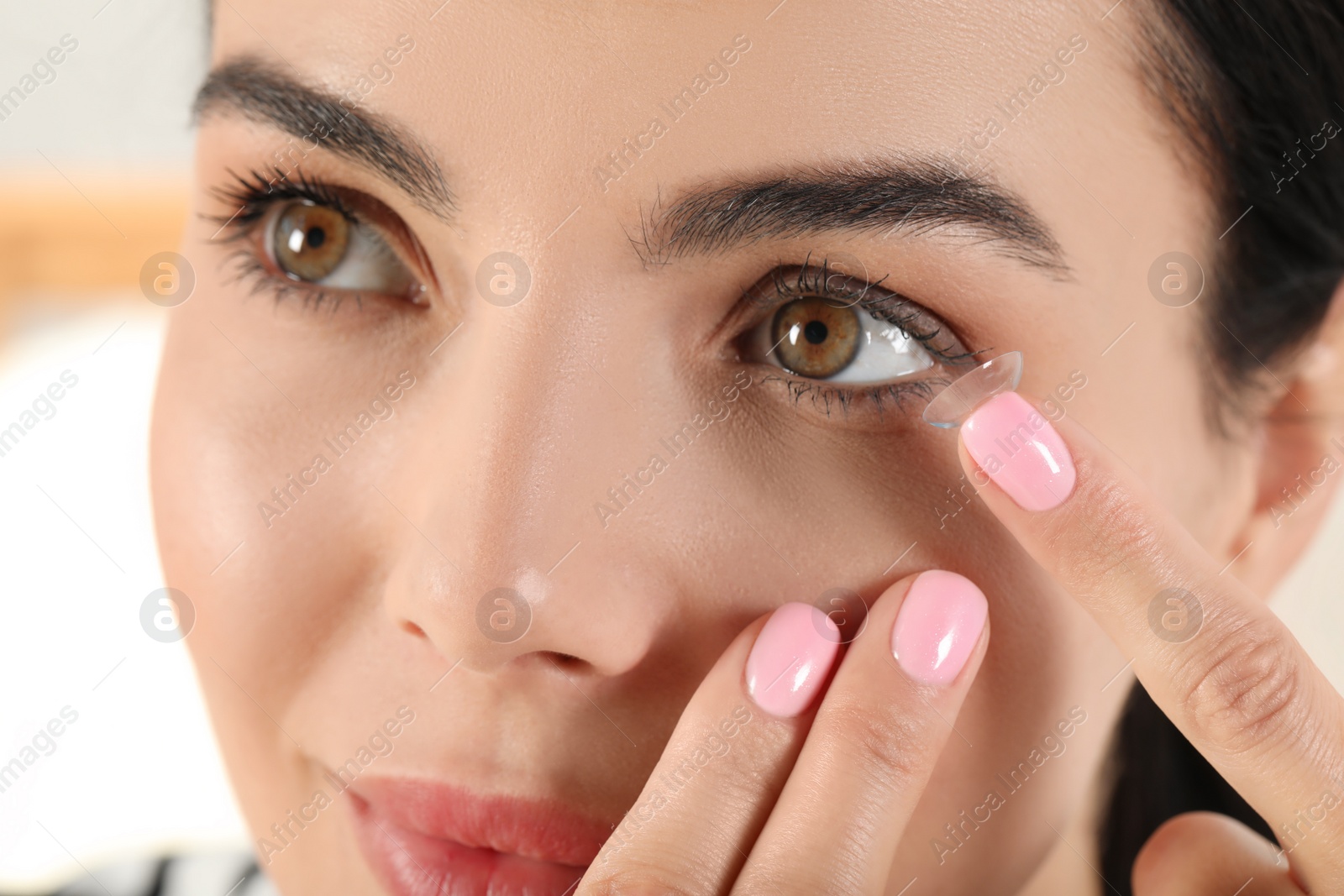 Photo of Young woman putting contact lens in her eye, closeup