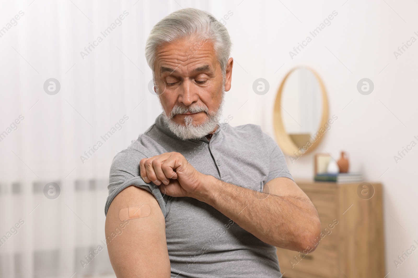 Photo of Senior man with adhesive bandage on his arm after vaccination at home
