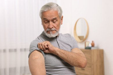 Senior man with adhesive bandage on his arm after vaccination at home