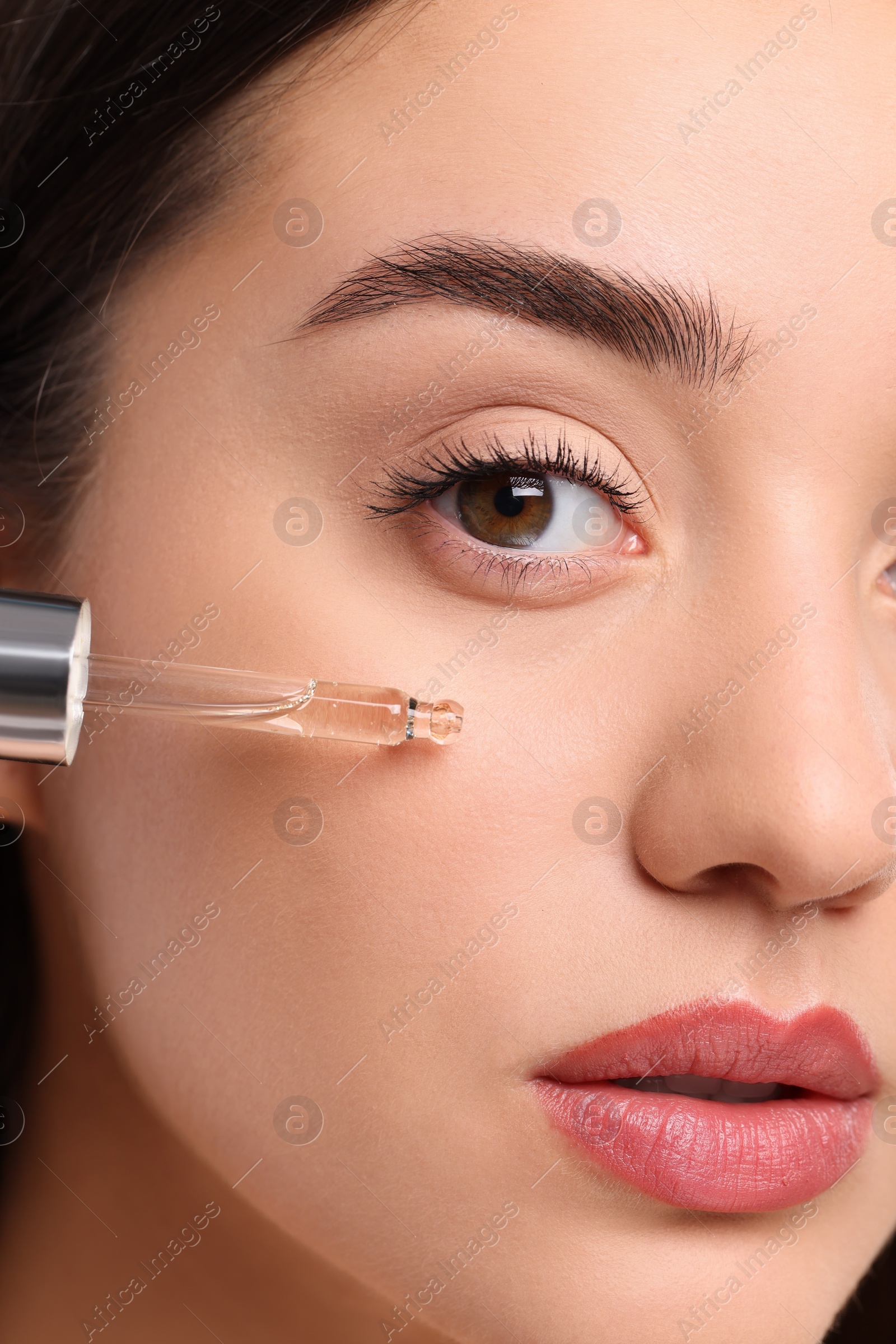 Photo of Young woman applying essential oil onto face, closeup