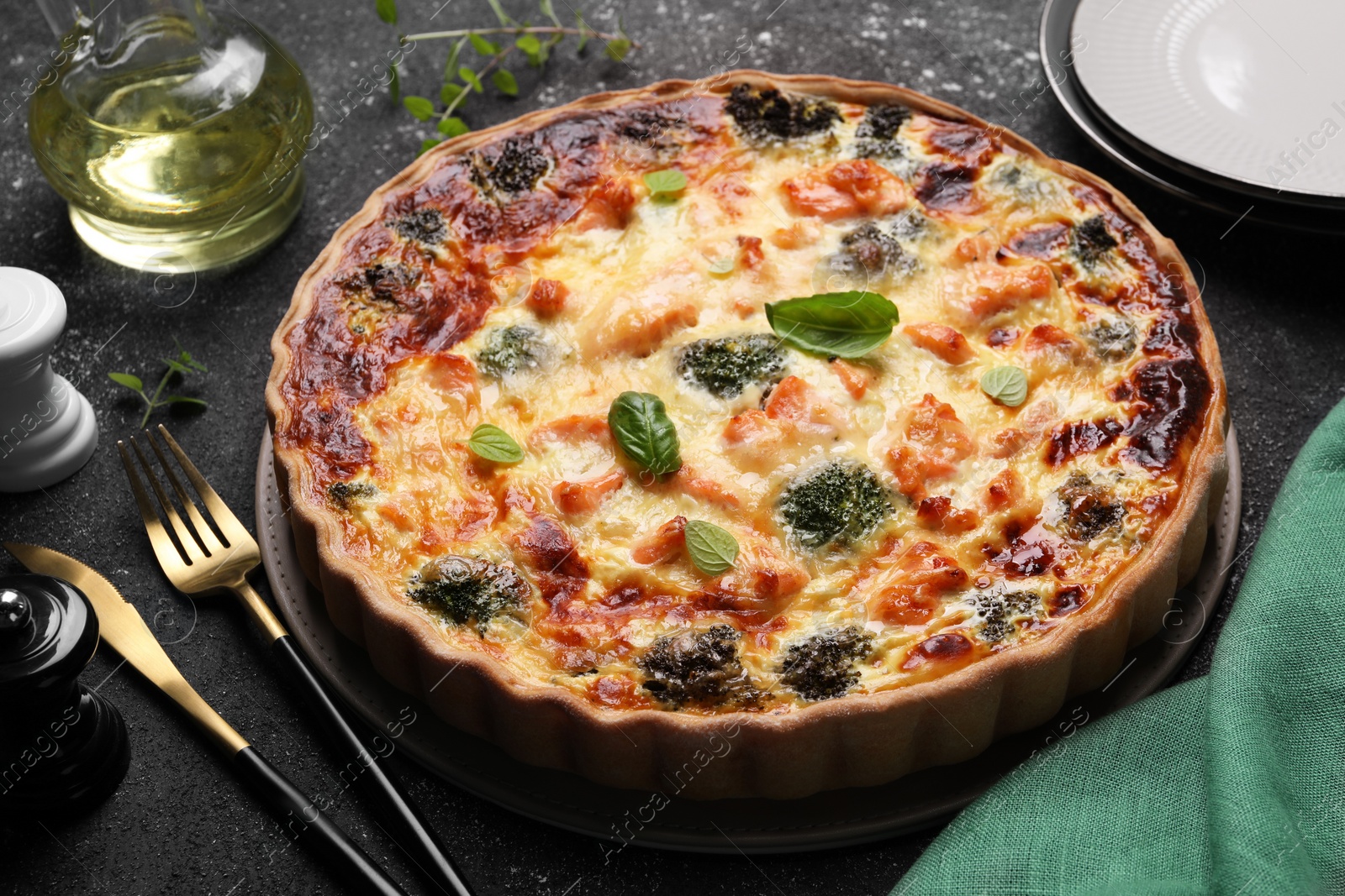 Photo of Delicious homemade salmon quiche with broccoli and cutlery on black table