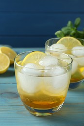 Delicious cocktails with lemon and ice balls on light blue wooden table