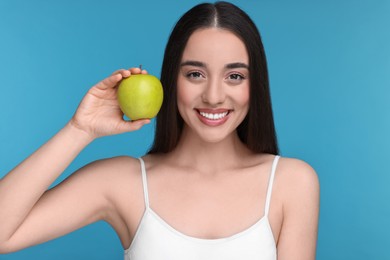 Beautiful young woman with apple on light blue background