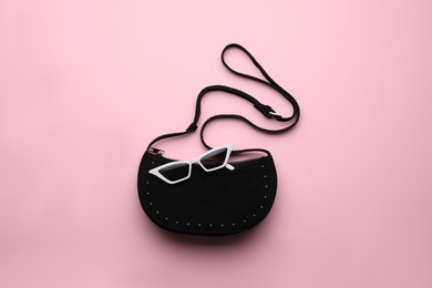 Stylish woman's bag and sunglasses on pink background, top view