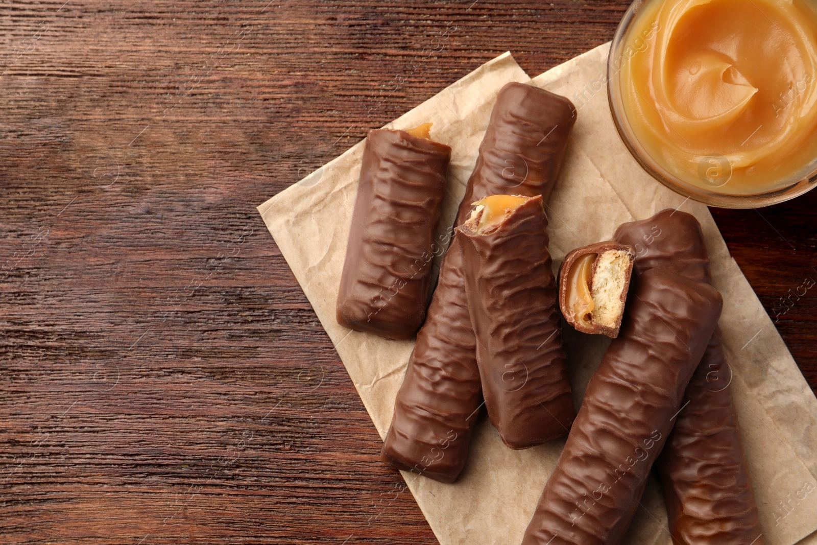 Photo of Sweet tasty chocolate bars with caramel on wooden table, top view. Space for text