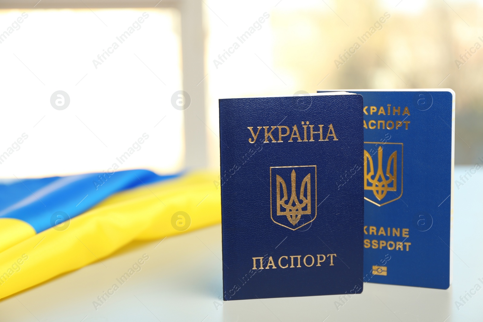 Photo of Ukrainian passports and national flag on table against blurred background, space for text. International relationships