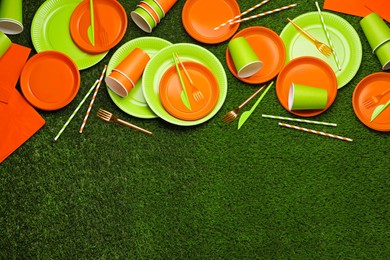 Photo of Disposable tableware on green artificial grass, flat lay. Space for text