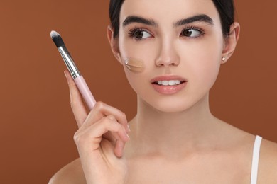 Photo of Teenage girl with swatch of foundation and makeup brush on brown background