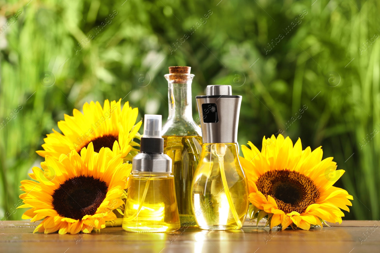 Photo of Sunflowers and many different bottles with cooking oil on wooden table against blurred green background