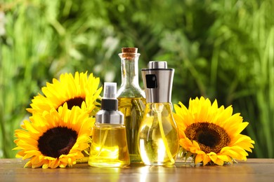 Sunflowers and many different bottles with cooking oil on wooden table against blurred green background