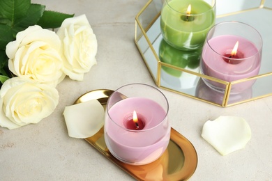 Burning candles in glass holders and roses on light table