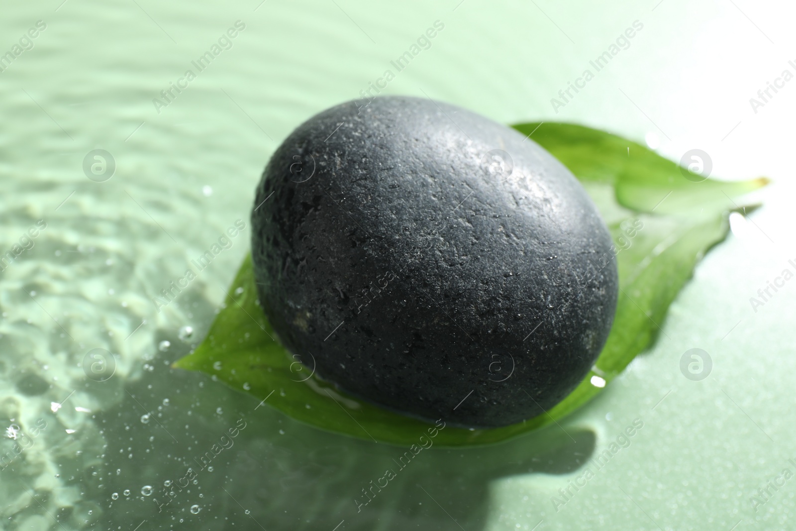 Photo of Spa stone and fresh leaf in water on light green background, closeup