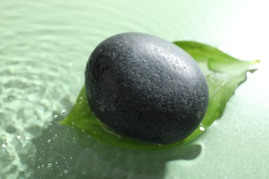 Photo of Spa stone and fresh leaf in water on light green background, closeup