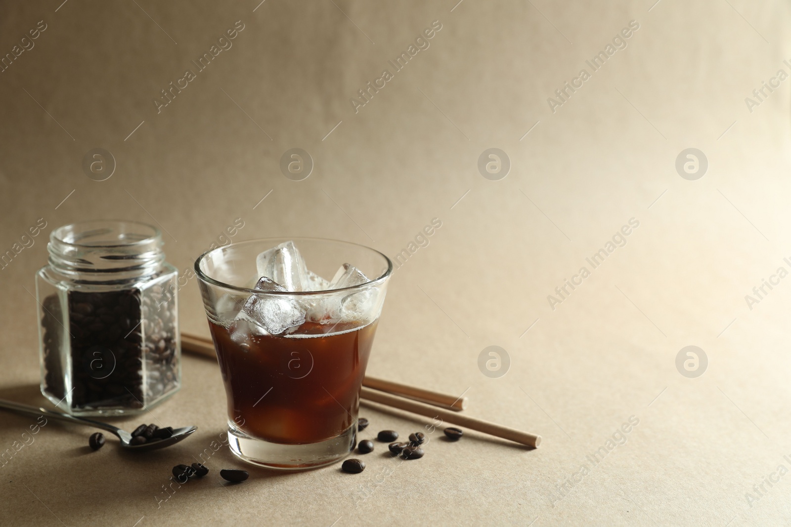 Photo of Refreshing iced coffee in glass, beans and straws on beige background. Space for text