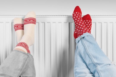 People warming feet near heating radiator, closeup