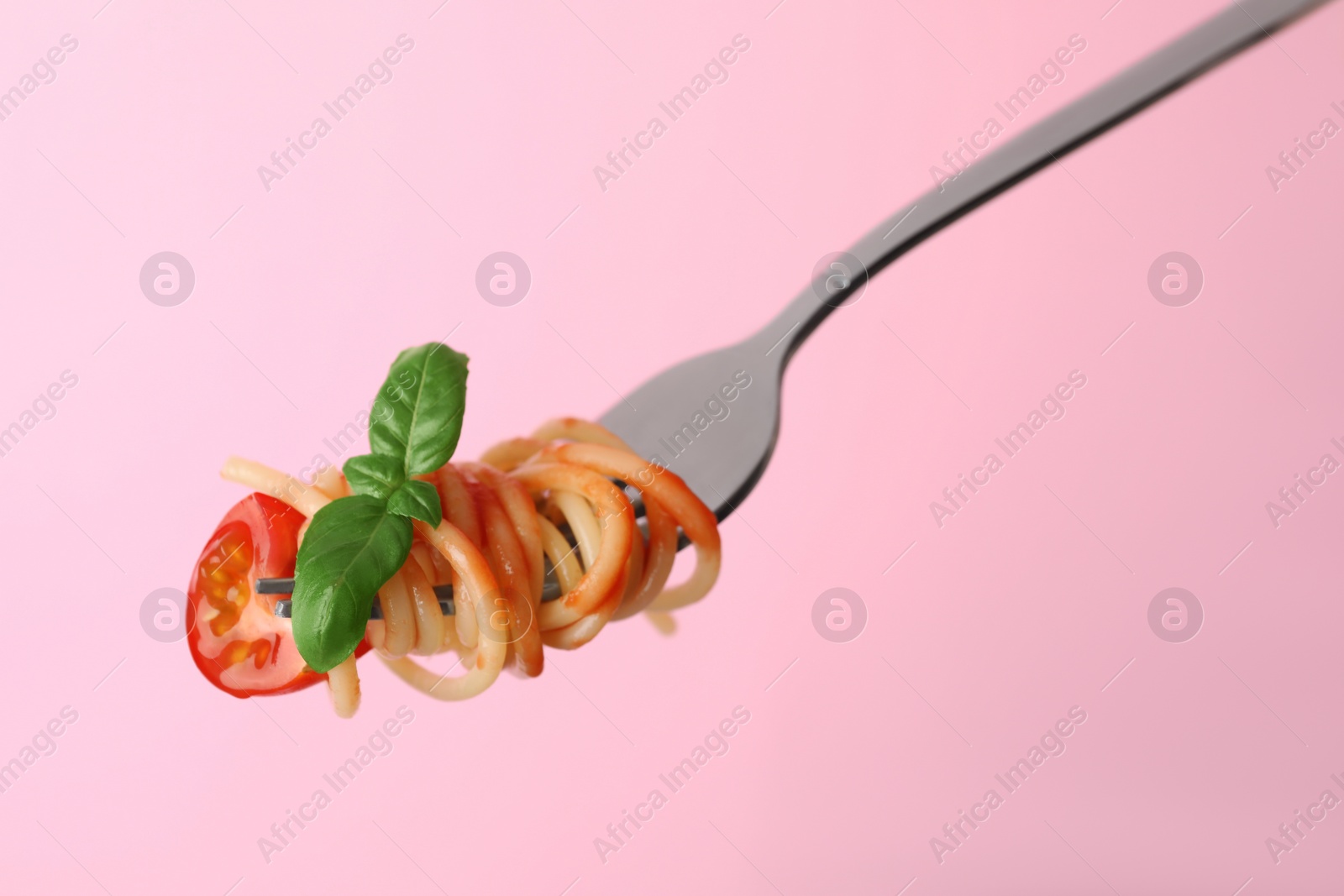 Photo of Tasty pasta with tomato sauce and basil on fork against pink background, closeup