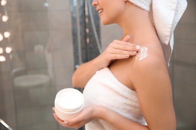 Photo of Beautiful woman with clean towels applying body cream in bathroom