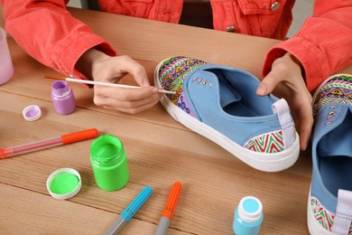 Photo of Woman painting on sneaker at wooden table, closeup. Customized shoes