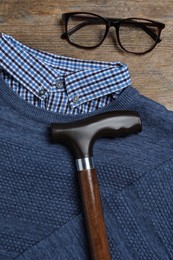 Elegant walking cane, glasses and sweater on wooden table, flat lay