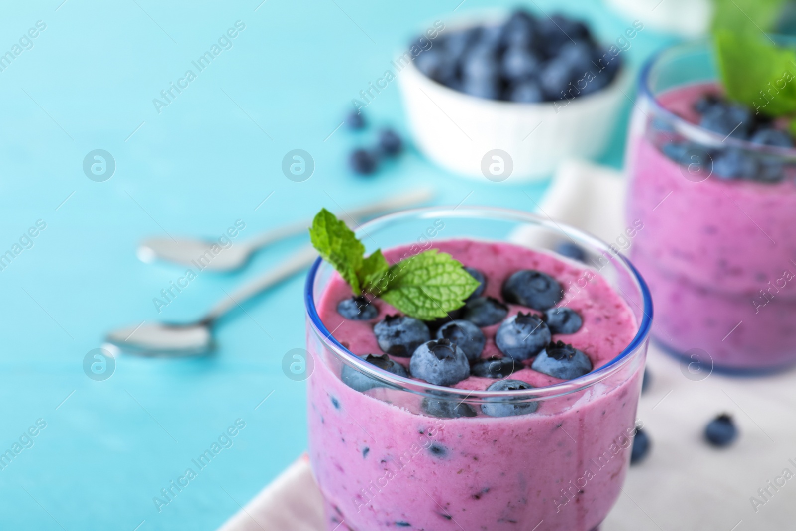 Photo of Glass of tasty blueberry smoothie and fabric on light blue table, closeup