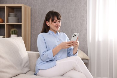 Beautiful young housewife using smartphone on sofa at home