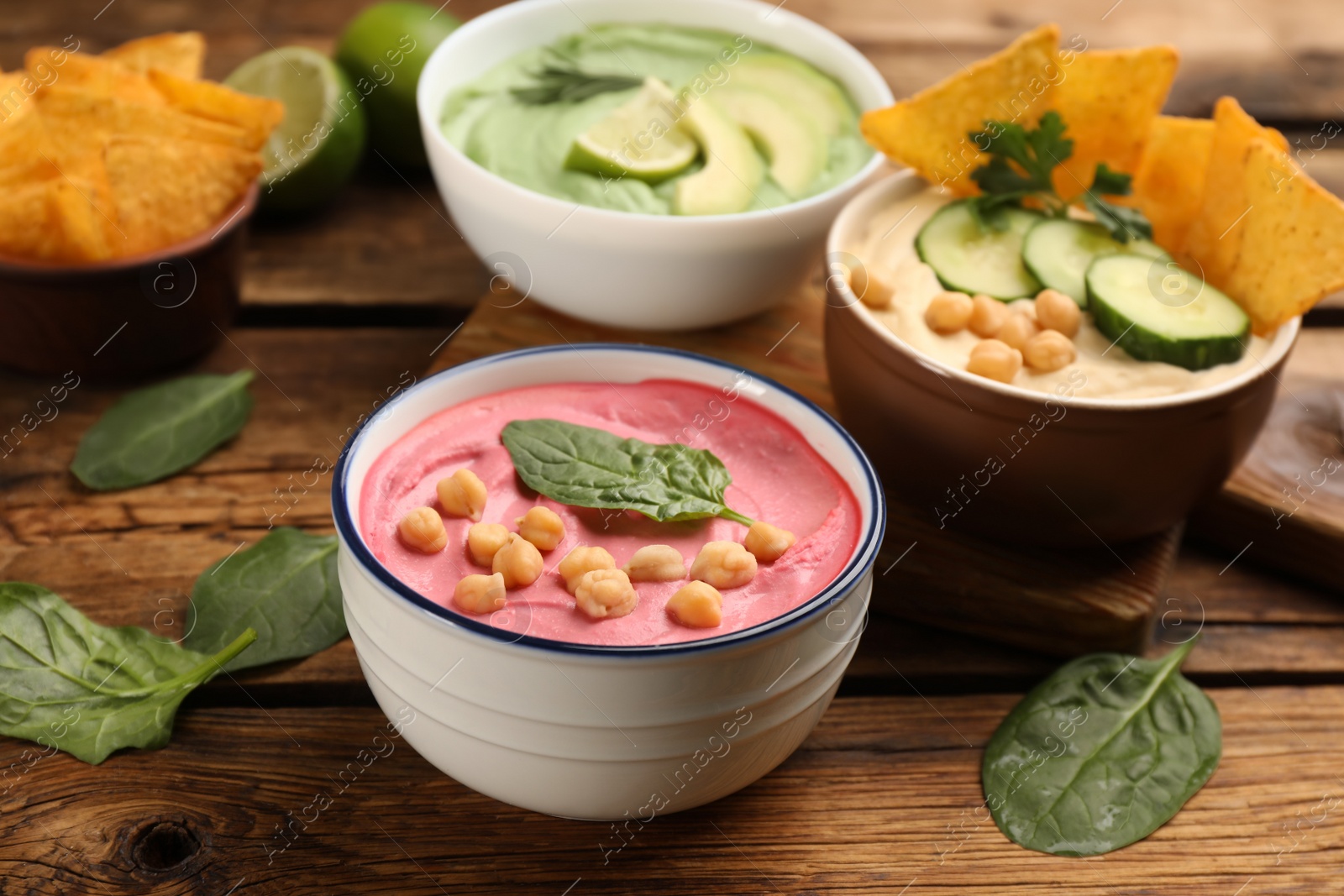 Photo of Bowl of delicious pink hummus with spinach on wooden table