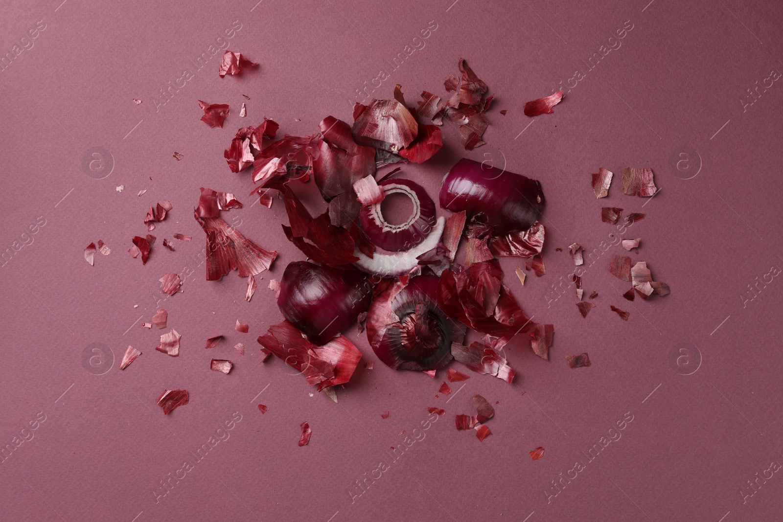 Photo of Peels of fresh red onion on dark pink background, top view